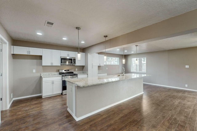 kitchen with light stone countertops, hanging light fixtures, a center island with sink, white cabinets, and appliances with stainless steel finishes