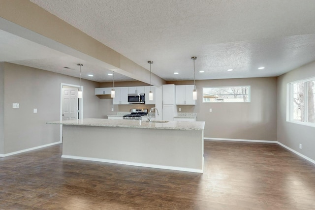 kitchen featuring light stone countertops, a textured ceiling, appliances with stainless steel finishes, decorative light fixtures, and white cabinetry