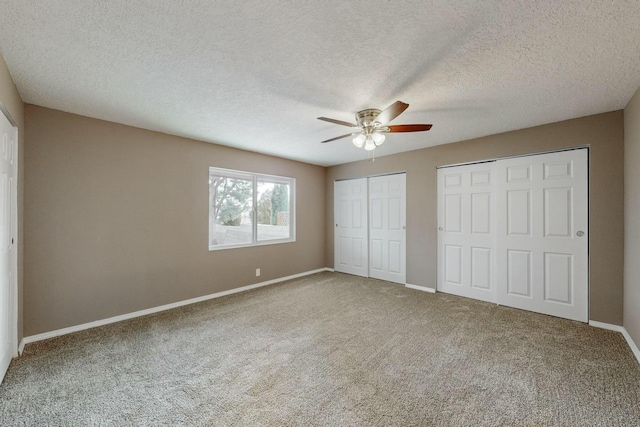 unfurnished bedroom with carpet, ceiling fan, a textured ceiling, and multiple closets