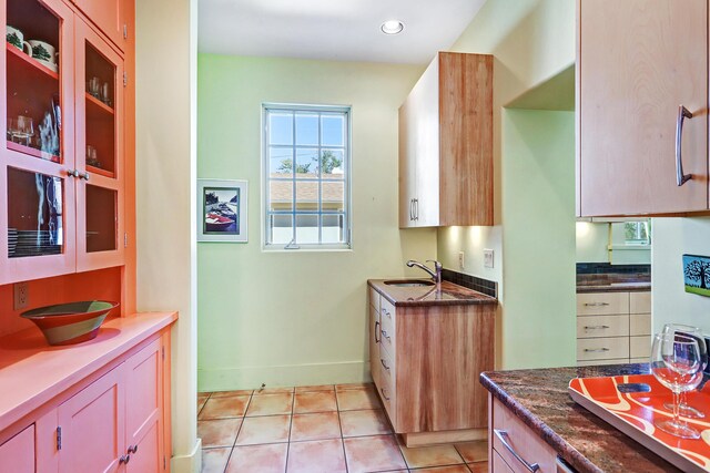 kitchen featuring light tile patterned floors, dark stone counters, and sink