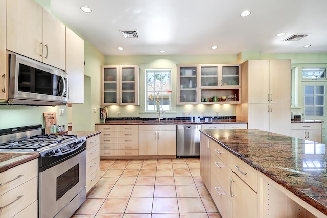 kitchen featuring light tile patterned floors, sink, appliances with stainless steel finishes, and dark stone counters