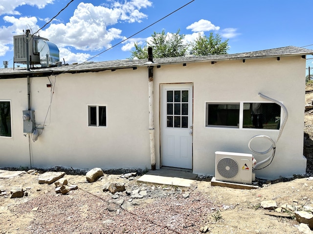 rear view of house featuring ac unit, a shingled roof, central AC unit, and stucco siding