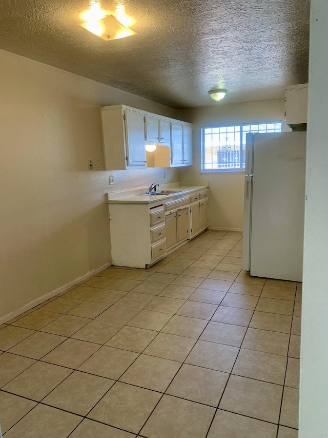 kitchen with a textured ceiling, sink, light tile patterned floors, white fridge, and white cabinetry