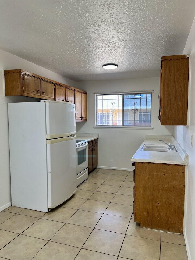 kitchen with light tile patterned floors, white appliances, a textured ceiling, and sink