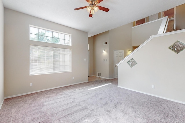 unfurnished living room featuring a towering ceiling, light colored carpet, and ceiling fan