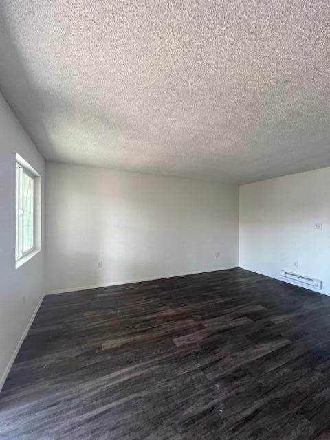 spare room with a textured ceiling, a baseboard radiator, and dark wood-type flooring