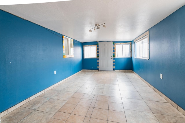 unfurnished room featuring light tile patterned floors, a textured ceiling, track lighting, and a wealth of natural light