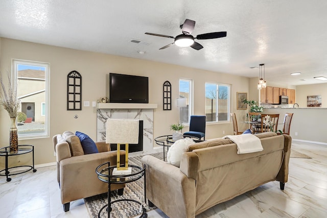 living room featuring a textured ceiling, ceiling fan, a fireplace, and a wealth of natural light