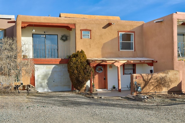 pueblo-style home featuring a garage, gravel driveway, and stucco siding