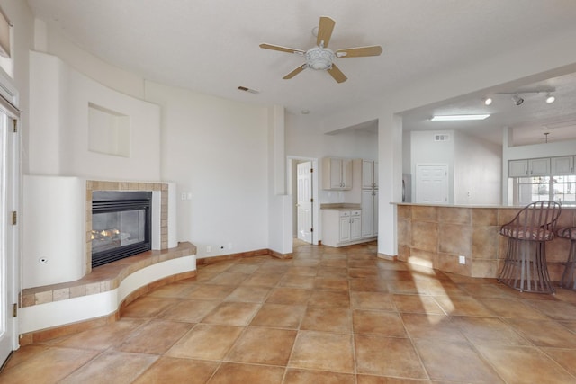 unfurnished living room featuring a tile fireplace, ceiling fan, and light tile patterned floors