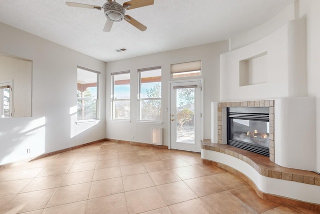 unfurnished living room with a tile fireplace, a textured ceiling, ceiling fan, and light tile patterned flooring