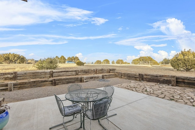 view of patio featuring outdoor dining area, a rural view, and fence