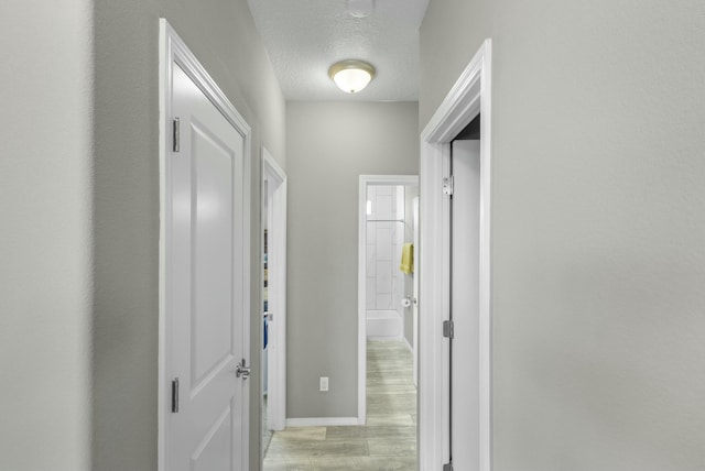 corridor featuring baseboards, light wood finished floors, and a textured ceiling