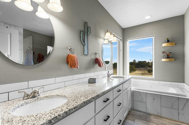 bathroom with a garden tub, double vanity, wood finished floors, a textured ceiling, and a sink