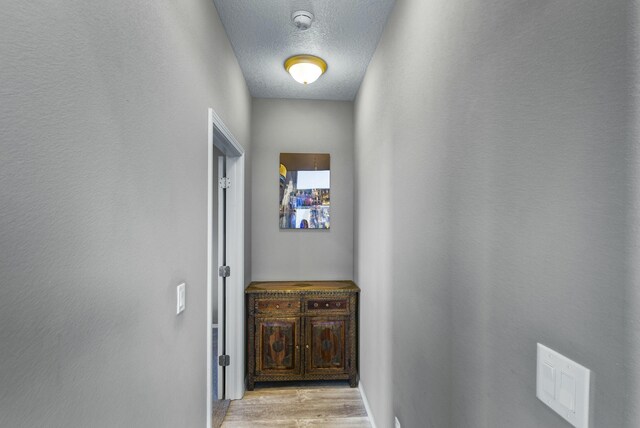 hallway with a textured wall, light wood finished floors, and a textured ceiling