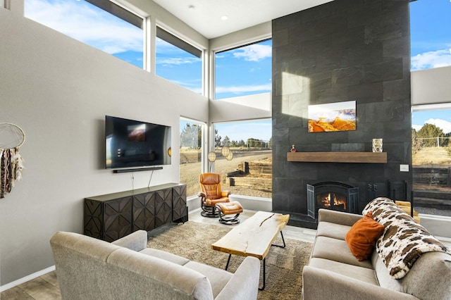 living room featuring a wealth of natural light, a tiled fireplace, baseboards, and wood finished floors