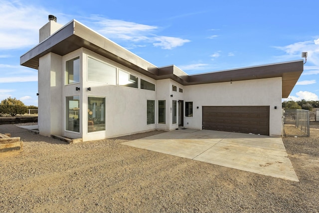 rear view of house featuring fence, a chimney, stucco siding, concrete driveway, and a garage