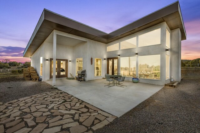 back of property at dusk with a patio area, stucco siding, and french doors