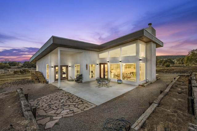 back of property at dusk with french doors, a patio, and stucco siding