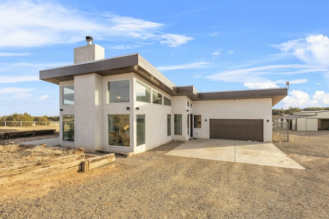 rear view of property with fence, stucco siding, a chimney, a garage, and driveway