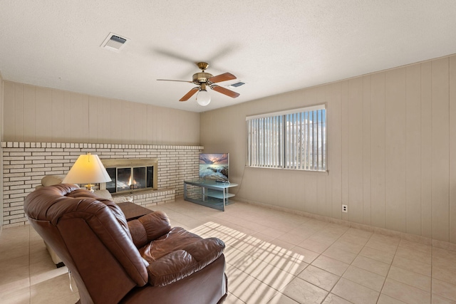 tiled living room featuring a brick fireplace and ceiling fan