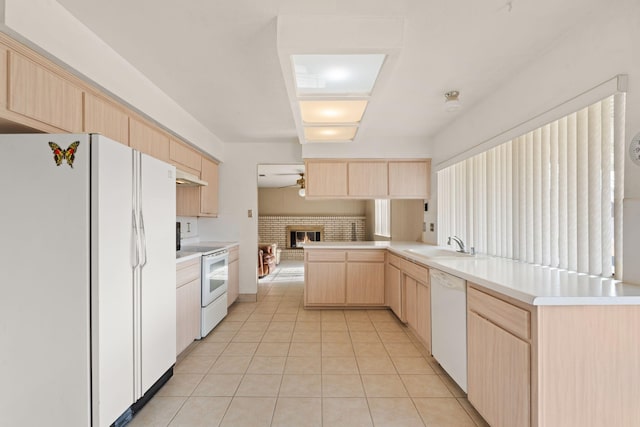 kitchen with light brown cabinets, white appliances, a brick fireplace, light tile patterned flooring, and kitchen peninsula