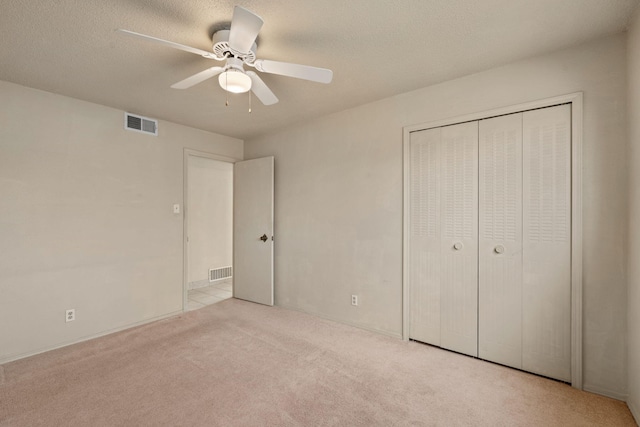 unfurnished bedroom featuring light carpet, a textured ceiling, a closet, and ceiling fan