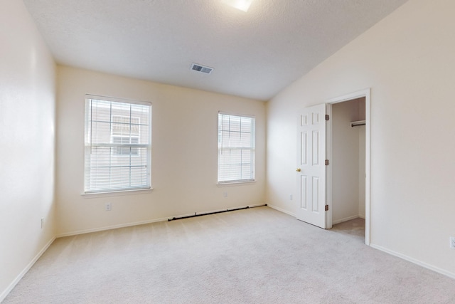 unfurnished bedroom featuring light carpet, a textured ceiling, vaulted ceiling, and a spacious closet