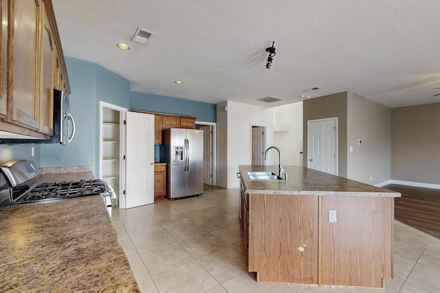 kitchen with a center island with sink, light tile patterned floors, sink, and appliances with stainless steel finishes