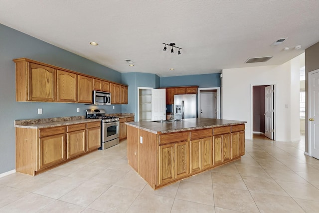 kitchen featuring appliances with stainless steel finishes, a textured ceiling, sink, light tile patterned floors, and an island with sink