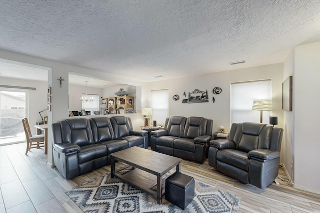 living room featuring visible vents, wood finish floors, an inviting chandelier, and a textured ceiling
