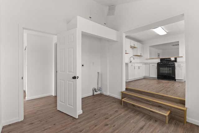 interior space with gas stove, white cabinetry, sink, and wood-type flooring