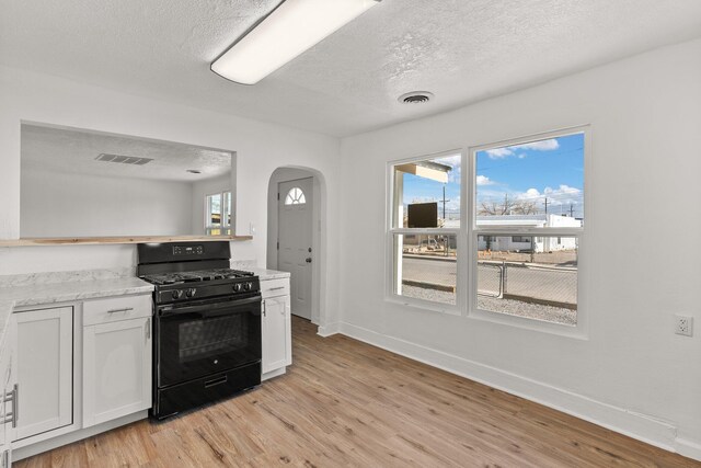 kitchen featuring black range with gas stovetop, white cabinetry, light wood-type flooring, and a wealth of natural light