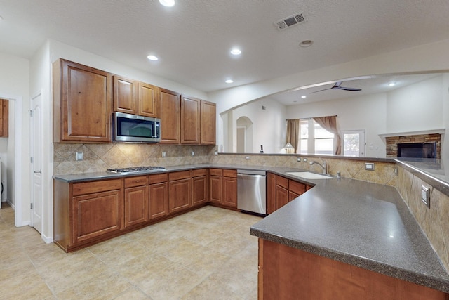 kitchen featuring backsplash, sink, ceiling fan, a fireplace, and appliances with stainless steel finishes