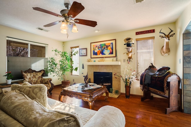 living room with a tiled fireplace, ceiling fan, and dark hardwood / wood-style flooring