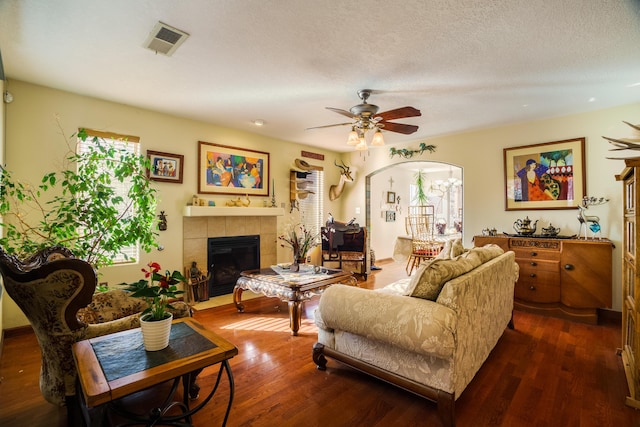 living room with ceiling fan, a fireplace, dark wood-type flooring, and a textured ceiling