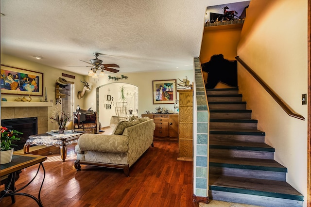 living room featuring a tile fireplace, ceiling fan, dark wood-type flooring, and a textured ceiling