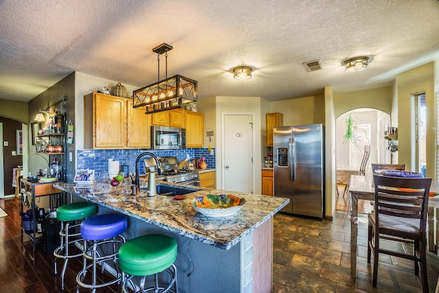 kitchen featuring light stone countertops, a textured ceiling, decorative light fixtures, decorative backsplash, and appliances with stainless steel finishes