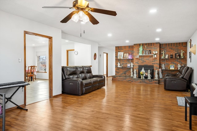 living room featuring hardwood / wood-style floors, a brick fireplace, and ceiling fan