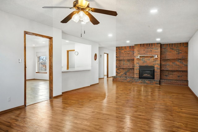 unfurnished living room featuring ceiling fan, a fireplace, a textured ceiling, and light wood-type flooring