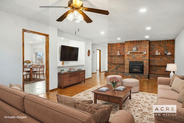 living room featuring a textured ceiling, light wood-type flooring, a brick fireplace, and ceiling fan