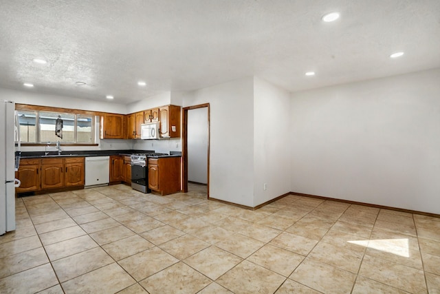 kitchen featuring sink, white appliances, a textured ceiling, and light tile patterned floors