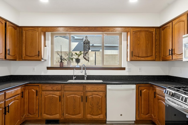 kitchen featuring dishwasher, stainless steel range oven, dark stone countertops, and sink