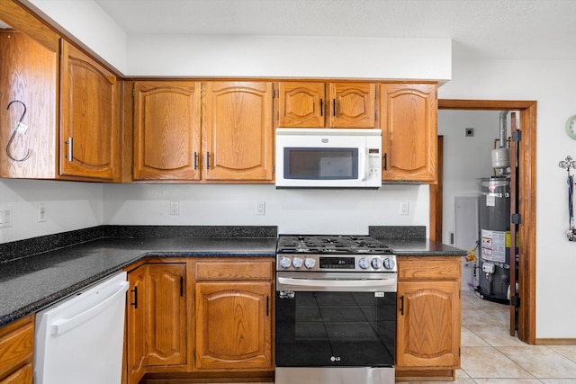 kitchen with water heater, light tile patterned flooring, dark stone counters, and white appliances