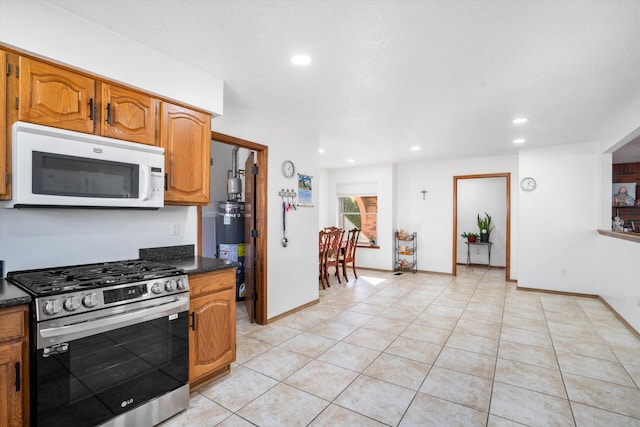 kitchen featuring secured water heater, stainless steel gas range oven, dark stone countertops, and light tile patterned floors