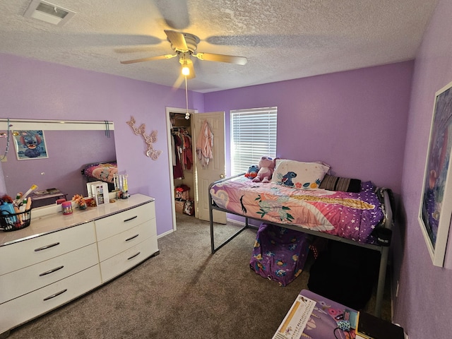 bedroom with carpet flooring, a walk in closet, ceiling fan, a textured ceiling, and a closet