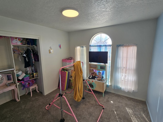 playroom featuring dark colored carpet and a textured ceiling