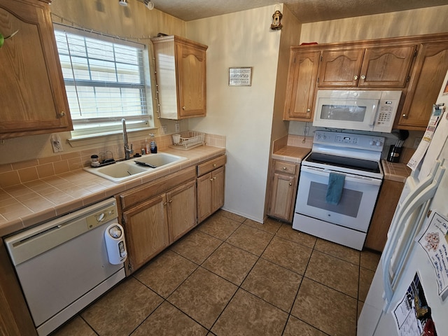 kitchen featuring white appliances, tile countertops, dark tile patterned flooring, a sink, and a textured ceiling