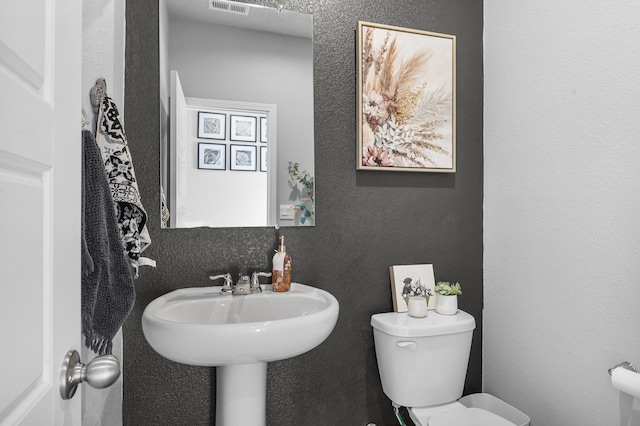 half bathroom featuring visible vents, toilet, and a textured wall