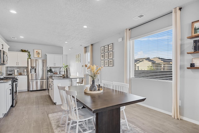 dining area with visible vents, baseboards, a textured ceiling, and light wood finished floors